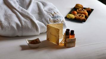 A neatly made bed with a white towel, a small bowl of cookies, and a box of Nuxe body soap.