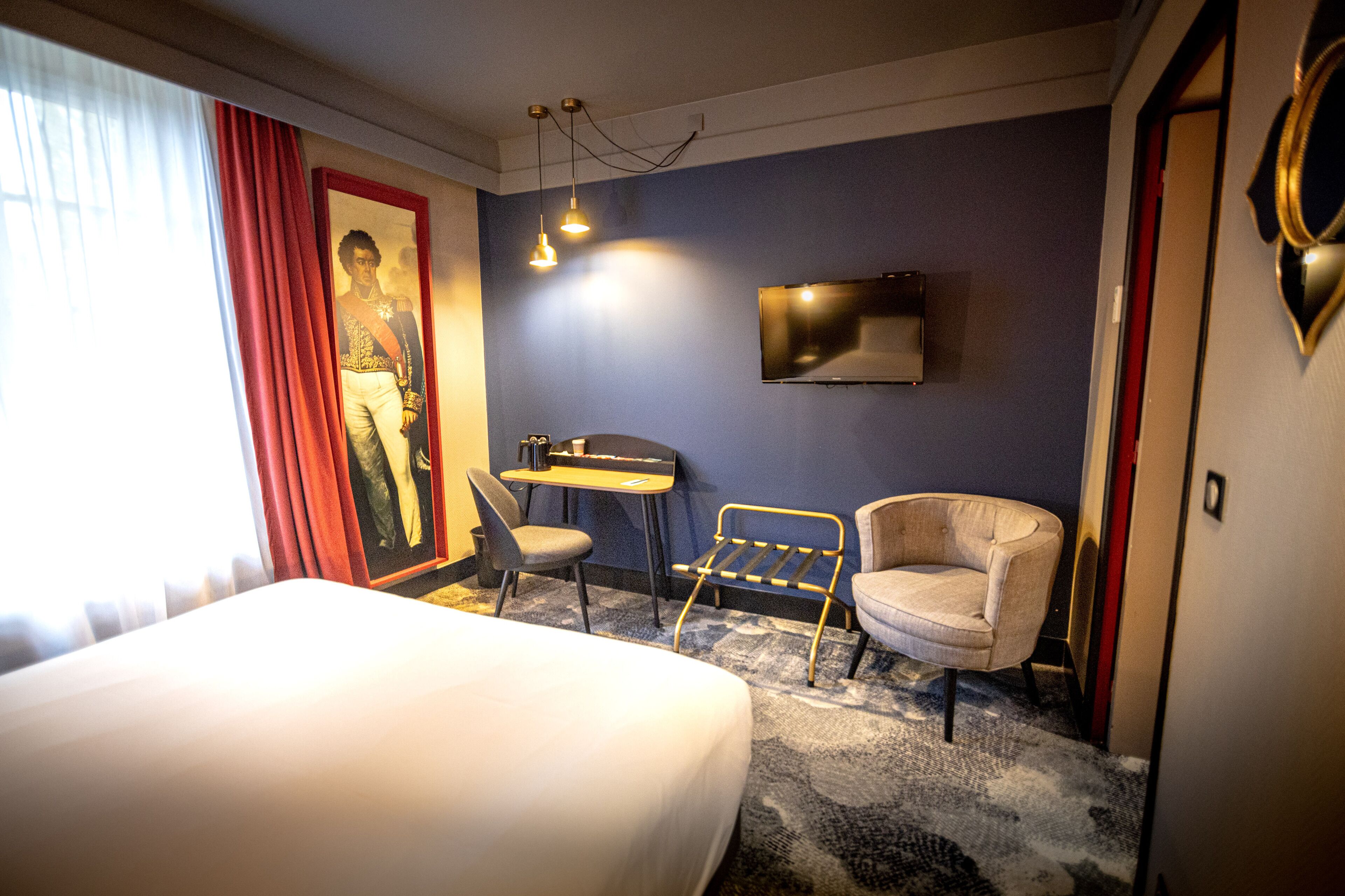 A hotel room with a bed, a desk, a chair, a TV, and a window with curtains.