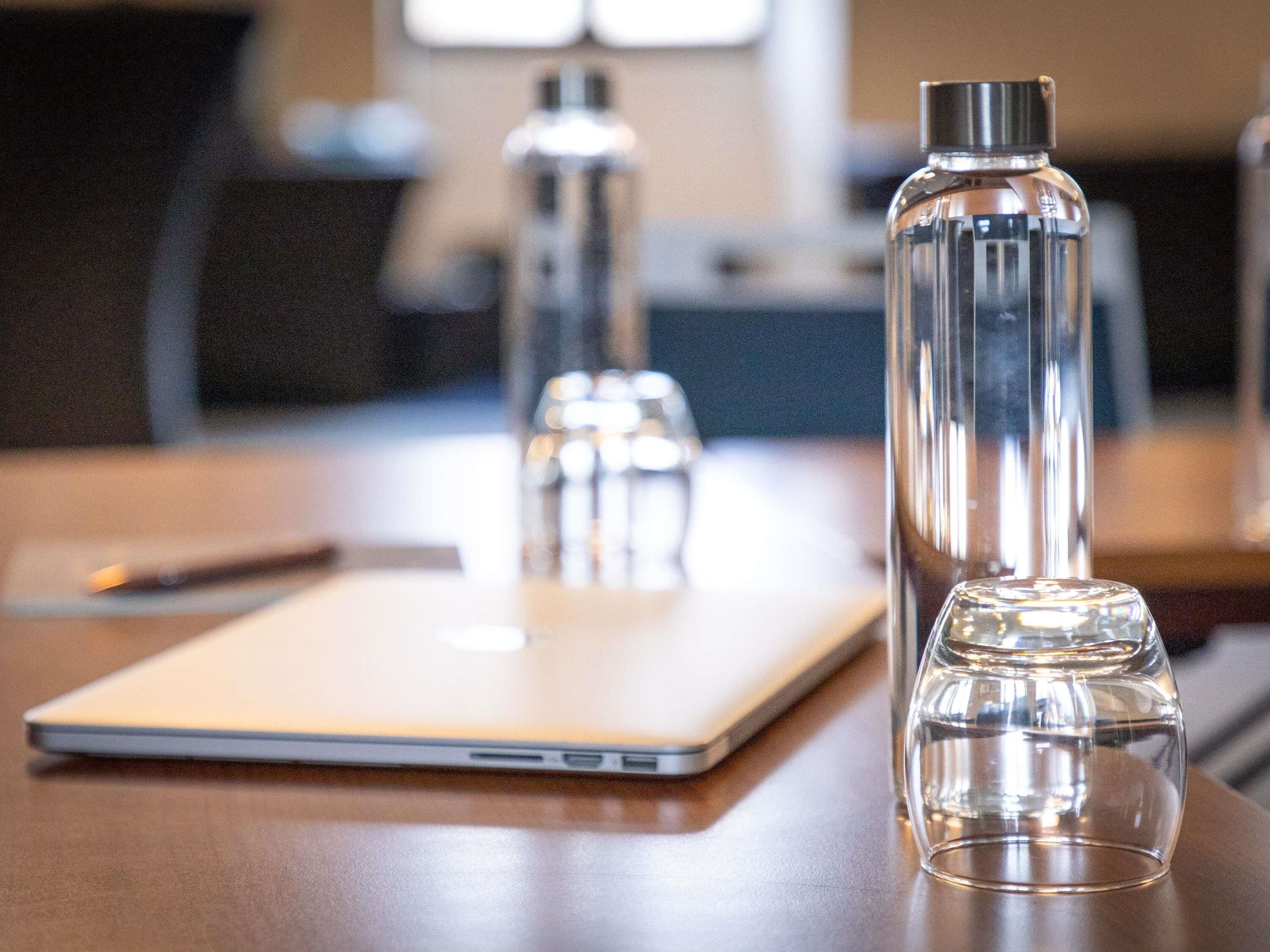 A laptop, a clear glass bottle, and a metal water bottle on a wooden table.