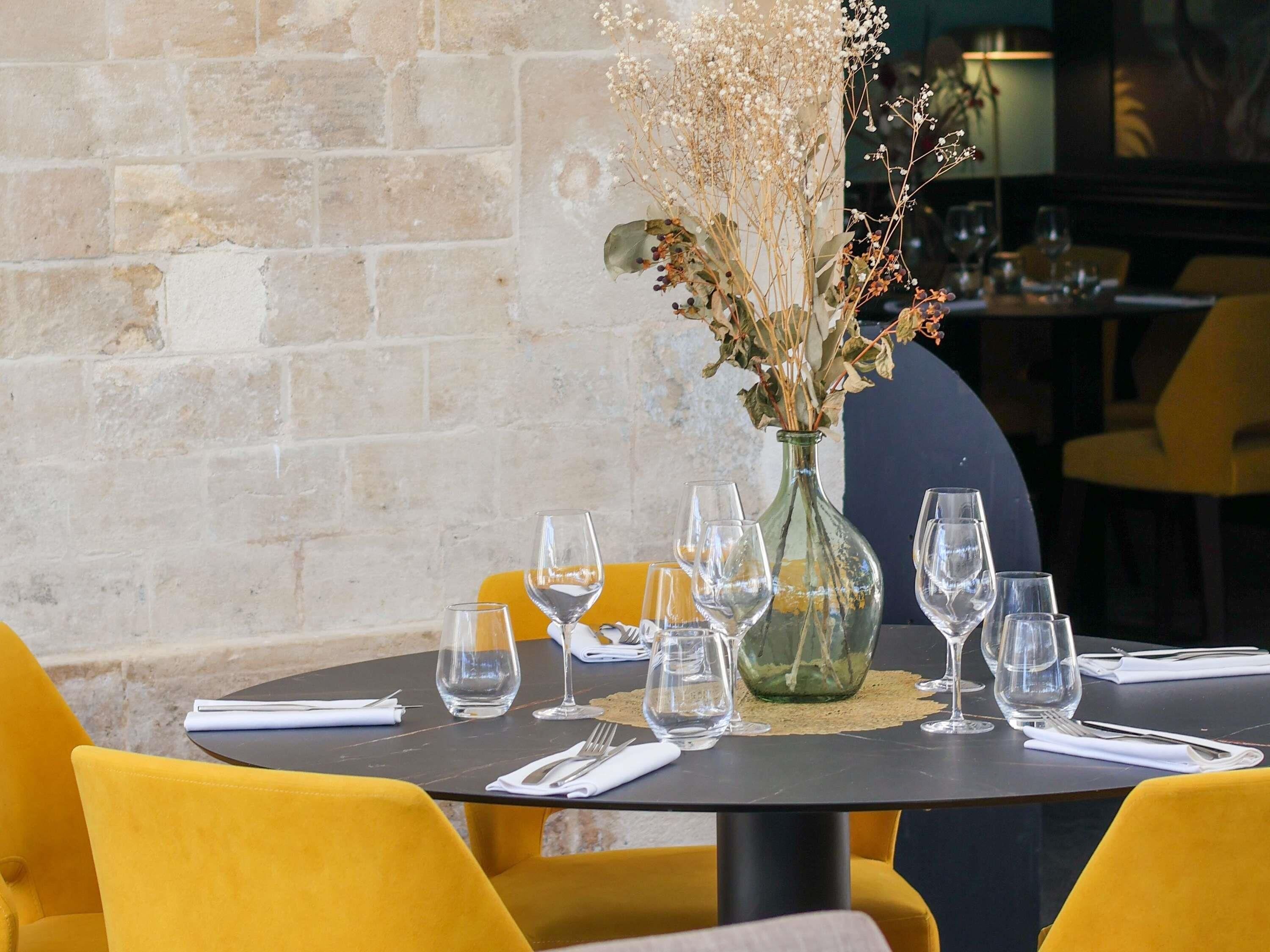 A dining table set with multiple wine glasses and a vase with dried flowers.