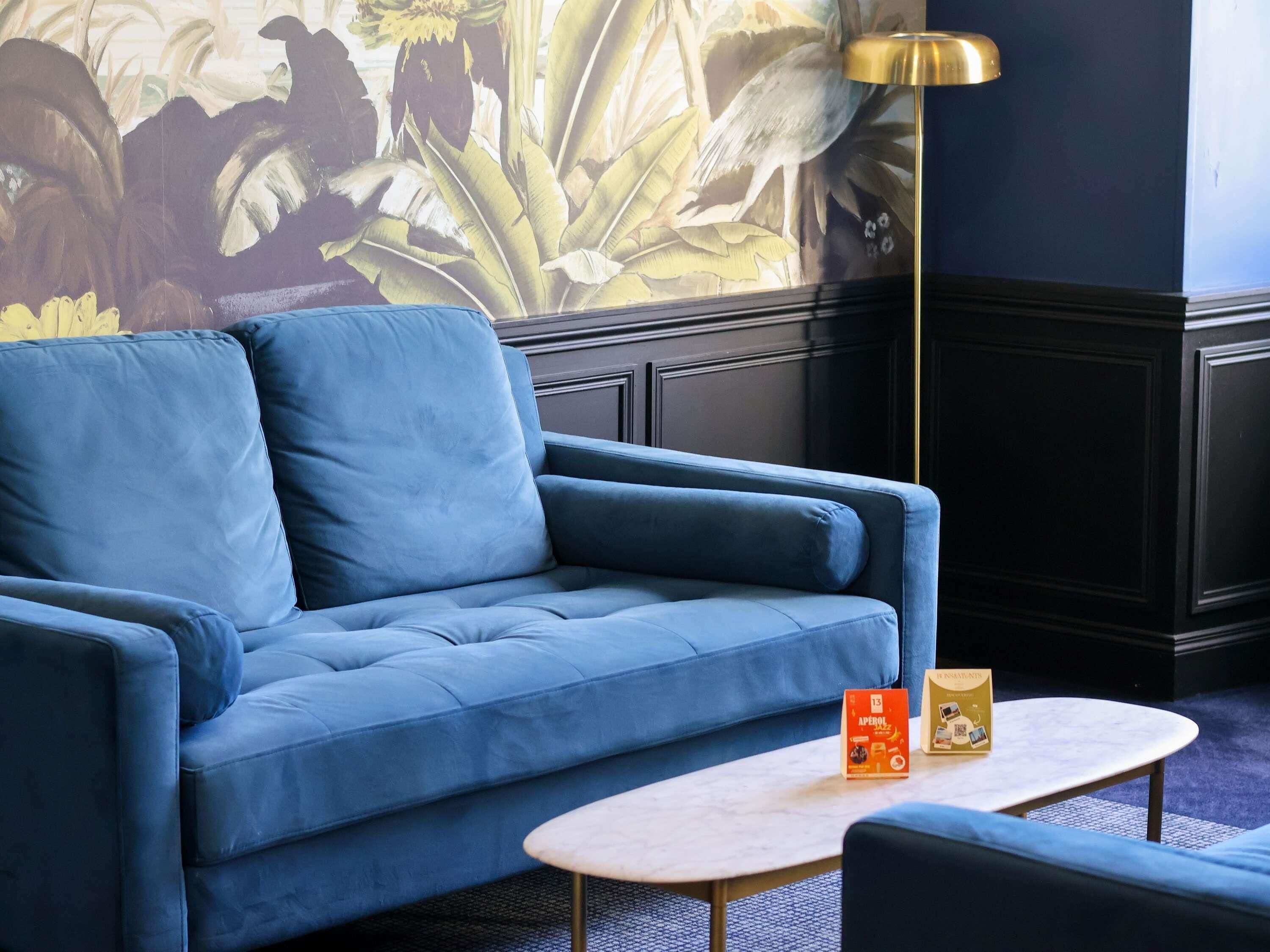 A blue sofa, a small round table, and a lamp in a room with a mural.