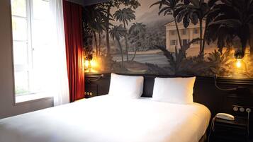 A hotel room with a large bed, a mural of tropical scenery on the wall, a window with red curtains, and bedside lamps.
