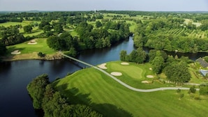 Een golfbaan met een rivier, bruggen en een vuurtoren in de verte.