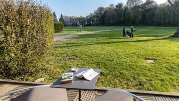 Vista de um terraço com vista para um campo de golfe, com uma mesa e cadeiras em primeiro plano.
