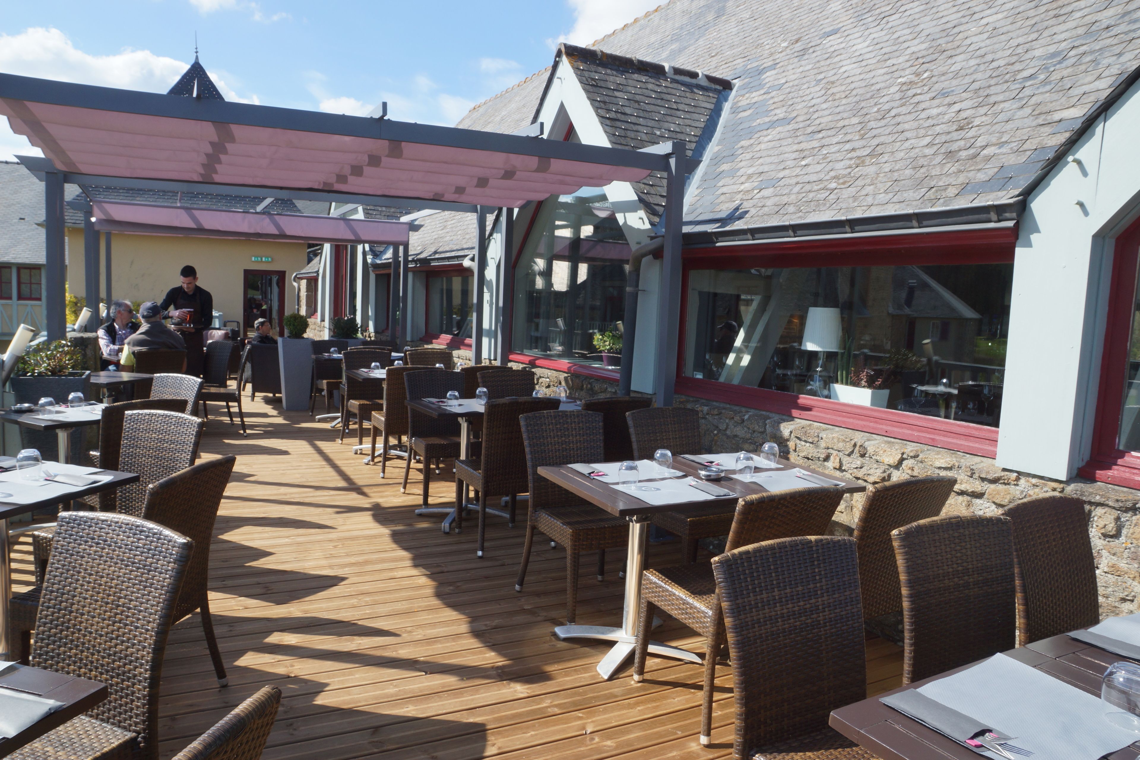 An outdoor dining area with wicker chairs and tables, a covered walkway, and a stone wall.