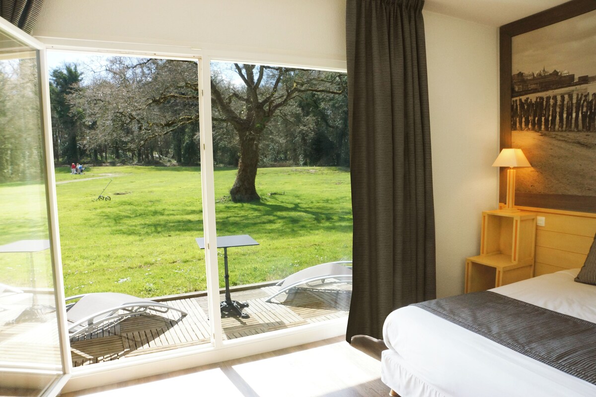 A bedroom with a large window, a bed, a nightstand, and a lamp.