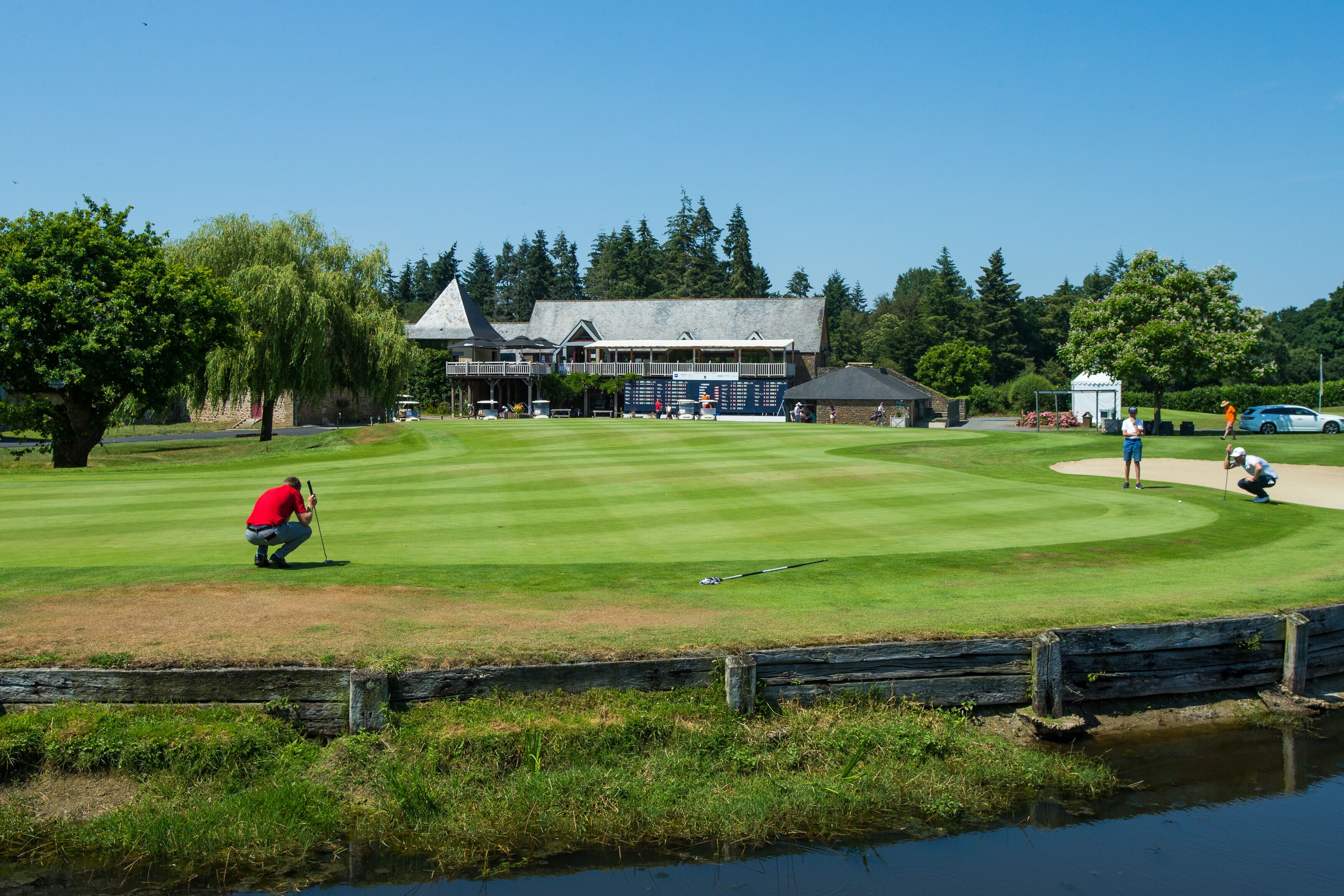 A golf course with a clubhouse, a pond, and a clear sky.