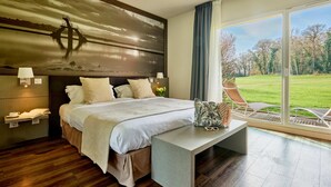Een moderne slaapkamer met een groot bed, nachtlampjes, een nachtkastje en uitzicht op een grasveld door grote ramen.