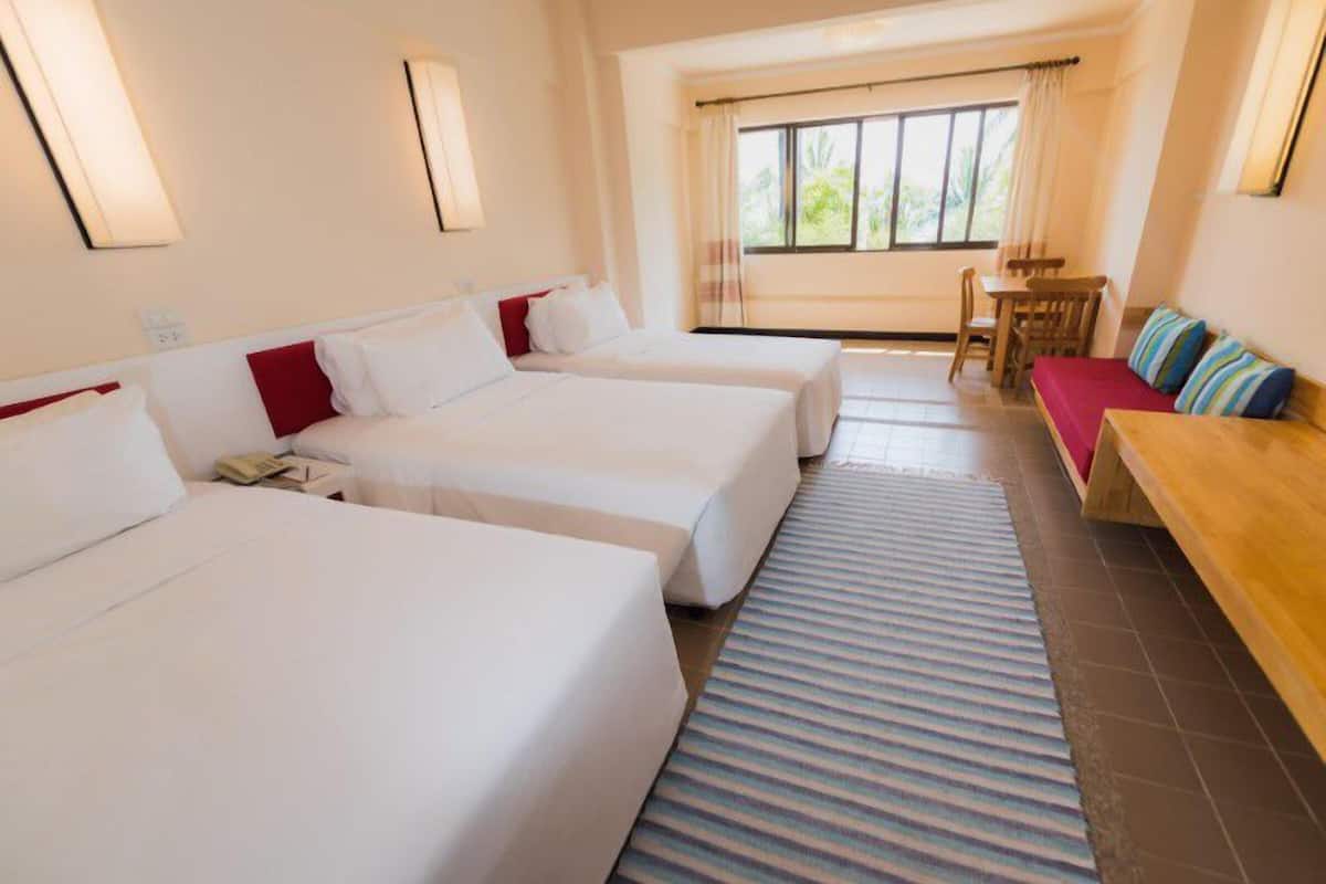 Una habitación de hotel con dos camas individuales, un sofá, una mesa de comedor y un ventanal con cortinas.