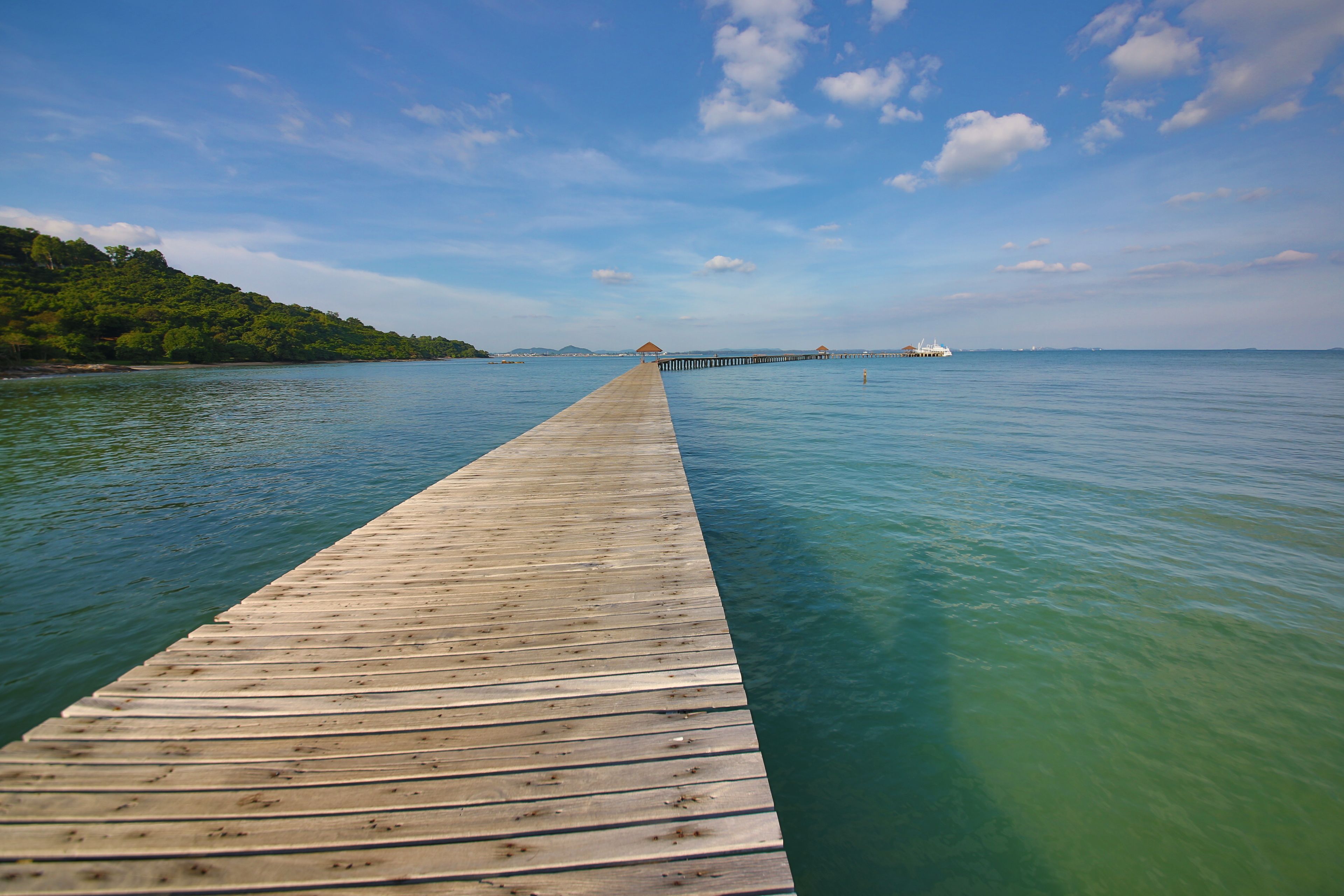 A wooden pier extending into clear blue water with a distant view of a small island and overwater bungalows.