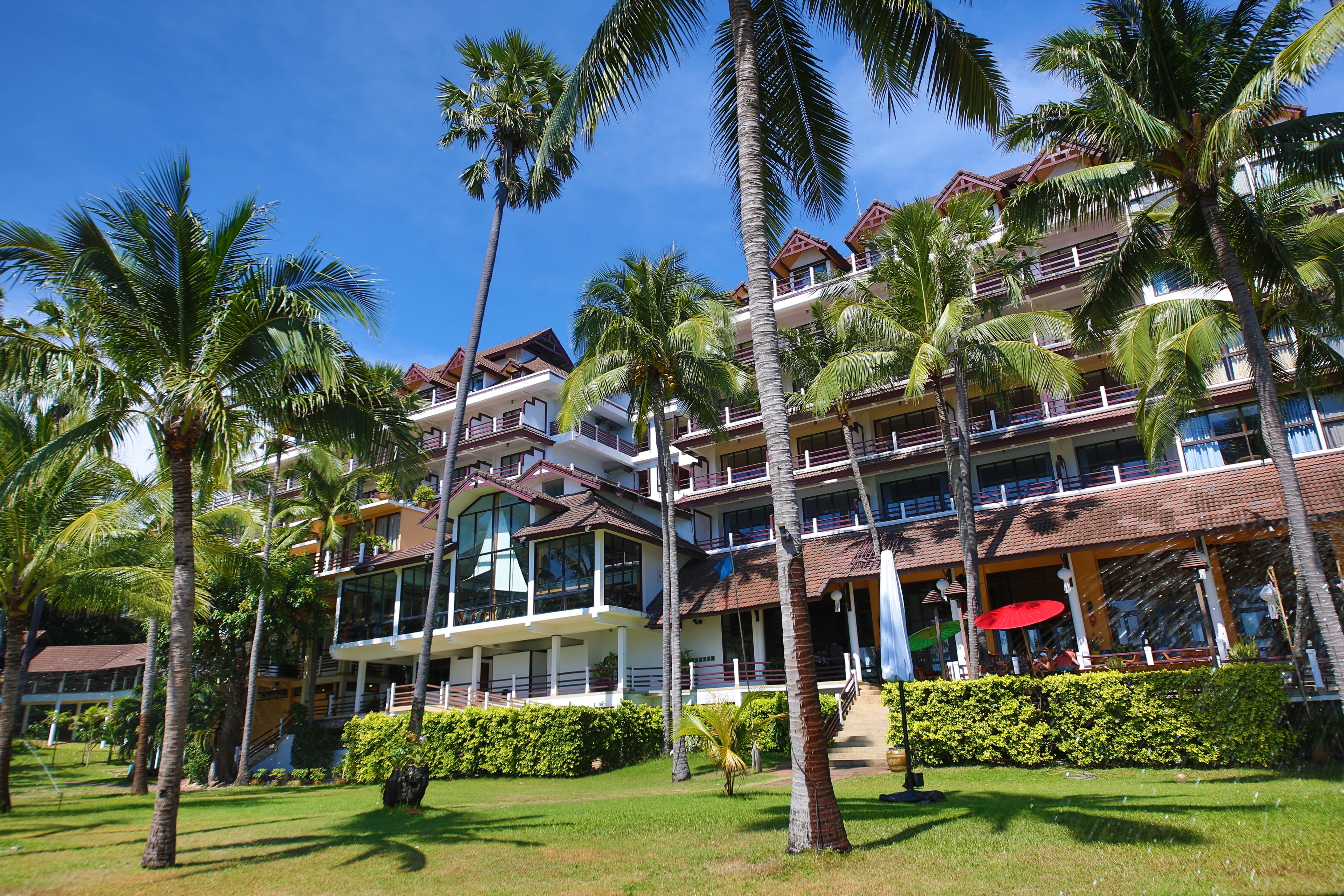 A multi-story hotel with balconies, palm trees, and a clear blue sky.