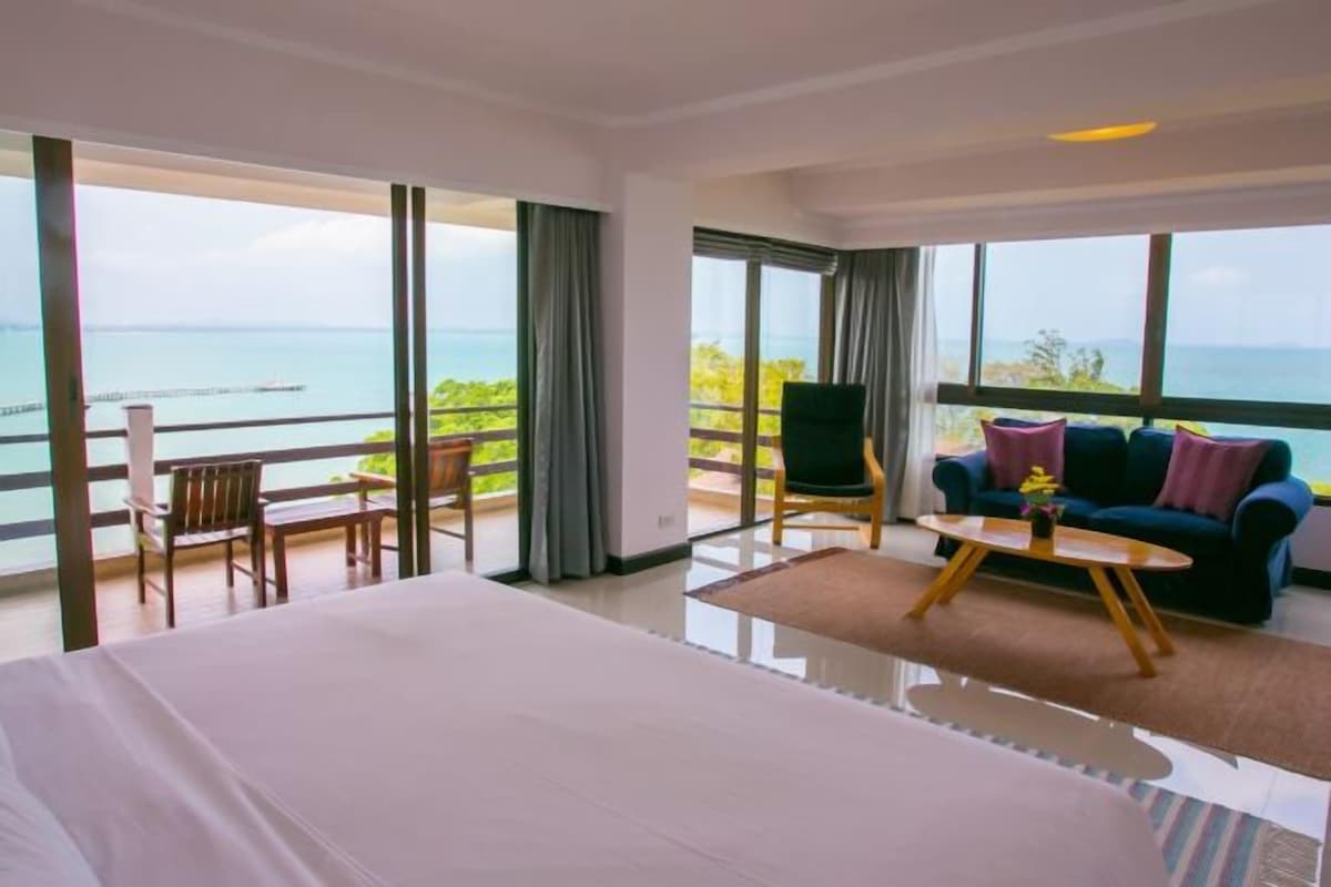 Habitación de hotel con una cama grande, un sofá, una mesa de centro y un balcón con vistas al mar.