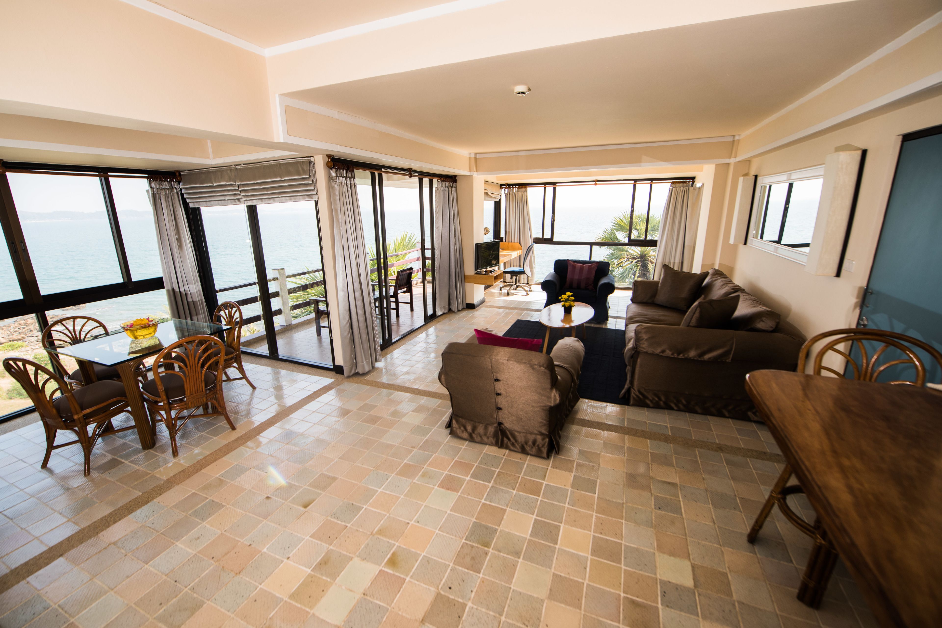 A spacious living area with a large window overlooking the sea, a dining table with chairs, and a sofa.