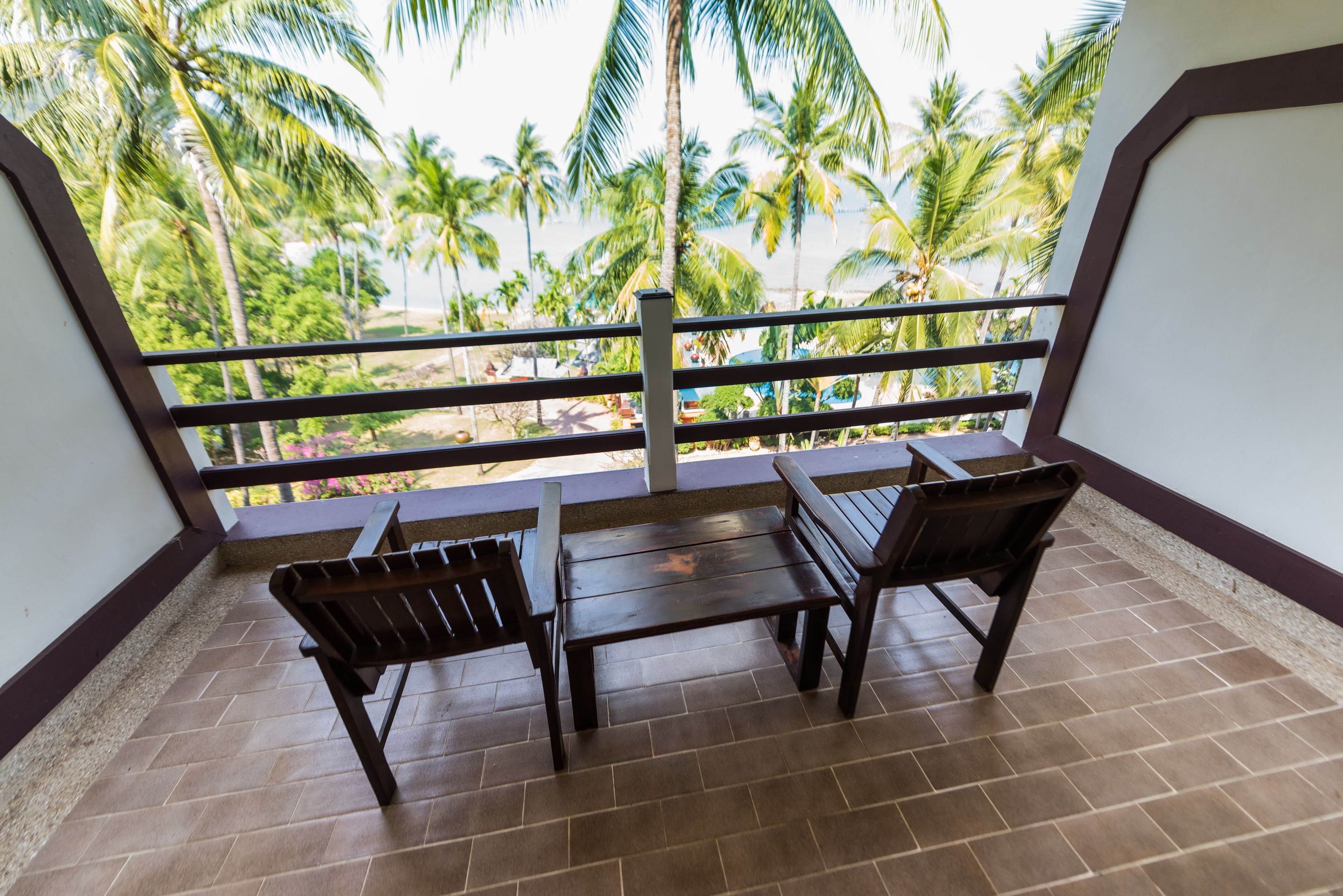 A balcony with two wooden benches and a view of palm trees.