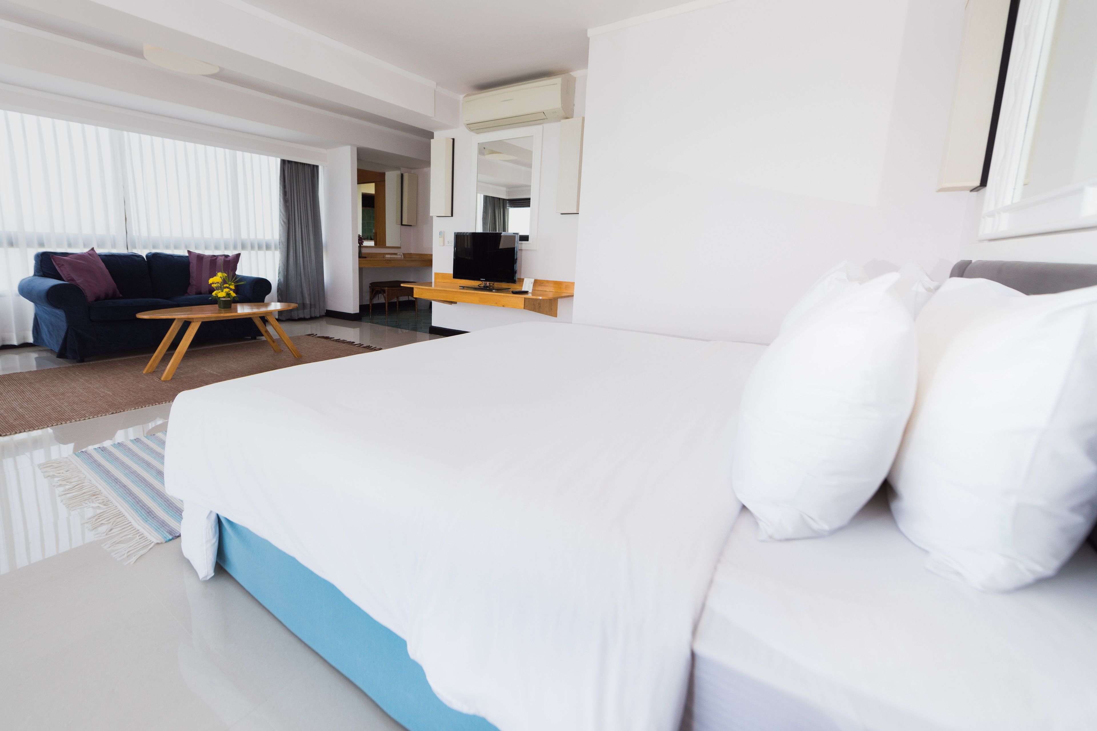 A modern hotel room with a large bed, a TV, a sofa, and a dining area.