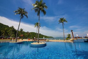 A clear blue pool with palm trees, lounge chairs, and a view of the sea.