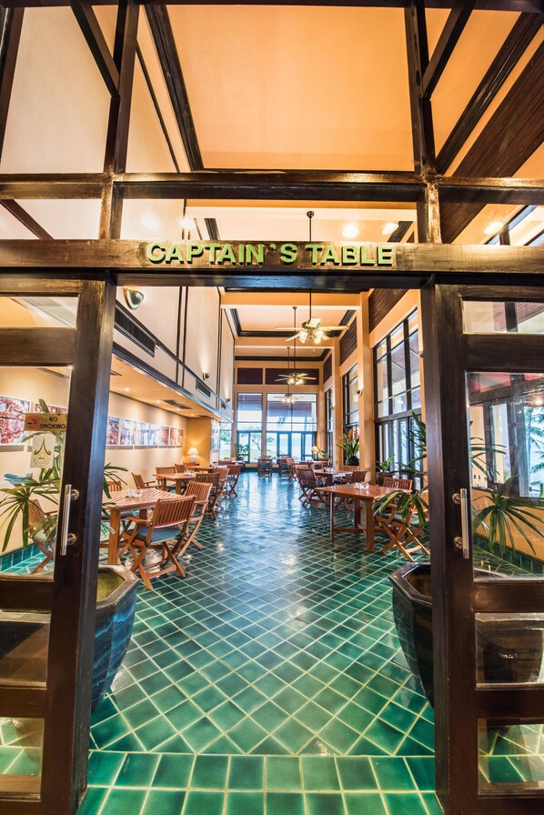 L’intérieur d’un restaurant avec un sol carrelé, des tables et des chaises en bois, et une enseigne indiquant « TABLE DU CAPITAINE ».