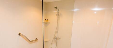 A modern bathroom with a glass-enclosed shower, a white toilet, and a handrail.
