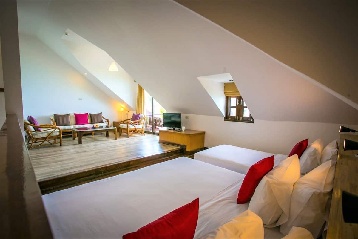 Habitación de hotel con dos camas, televisión, escritorio y zona de estar con sillas y una mesa.