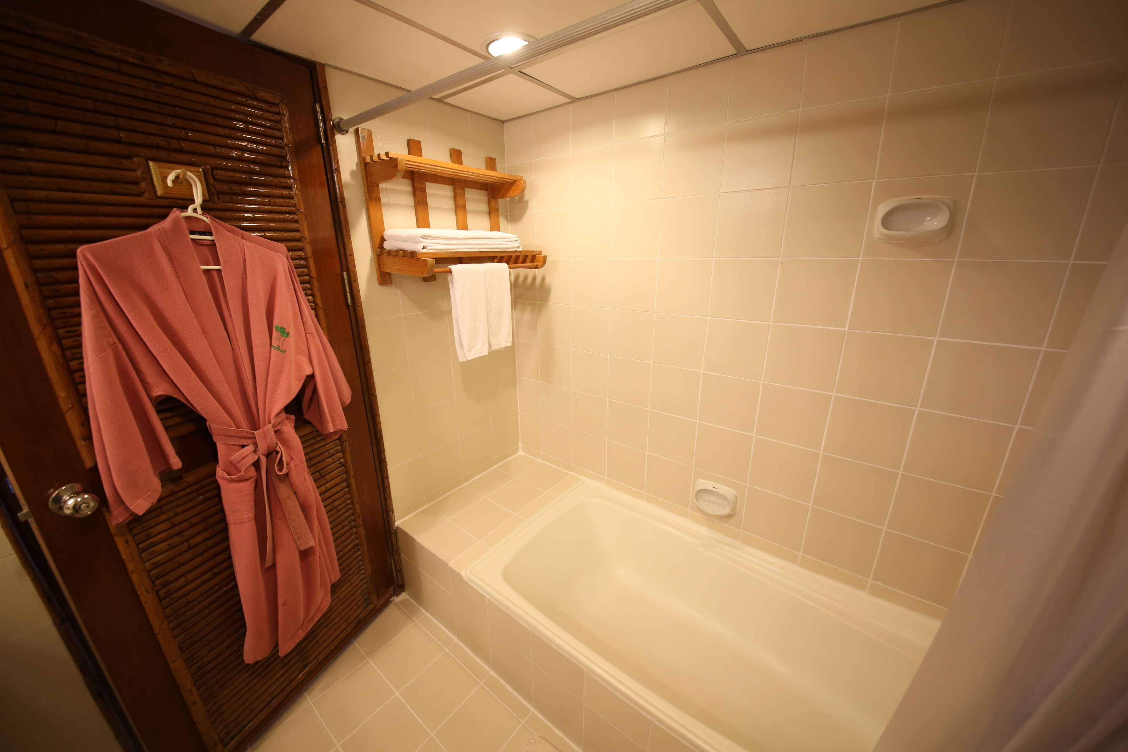 Un baño con puerta de madera, bañera y toallero con batas.