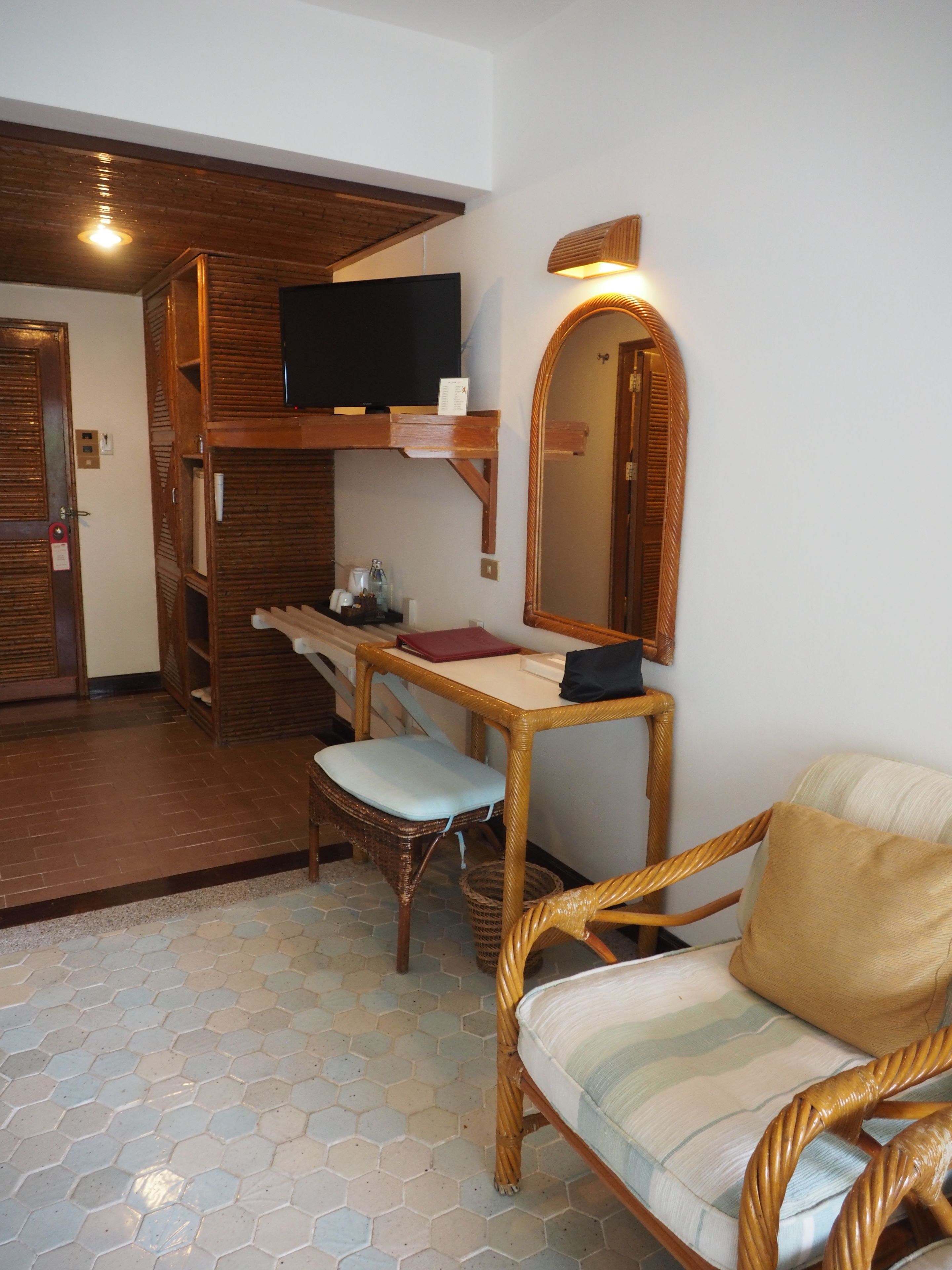 Une pièce de taille modeste, comprenant un bureau en bois, une chaise, un téléviseur et un miroir.