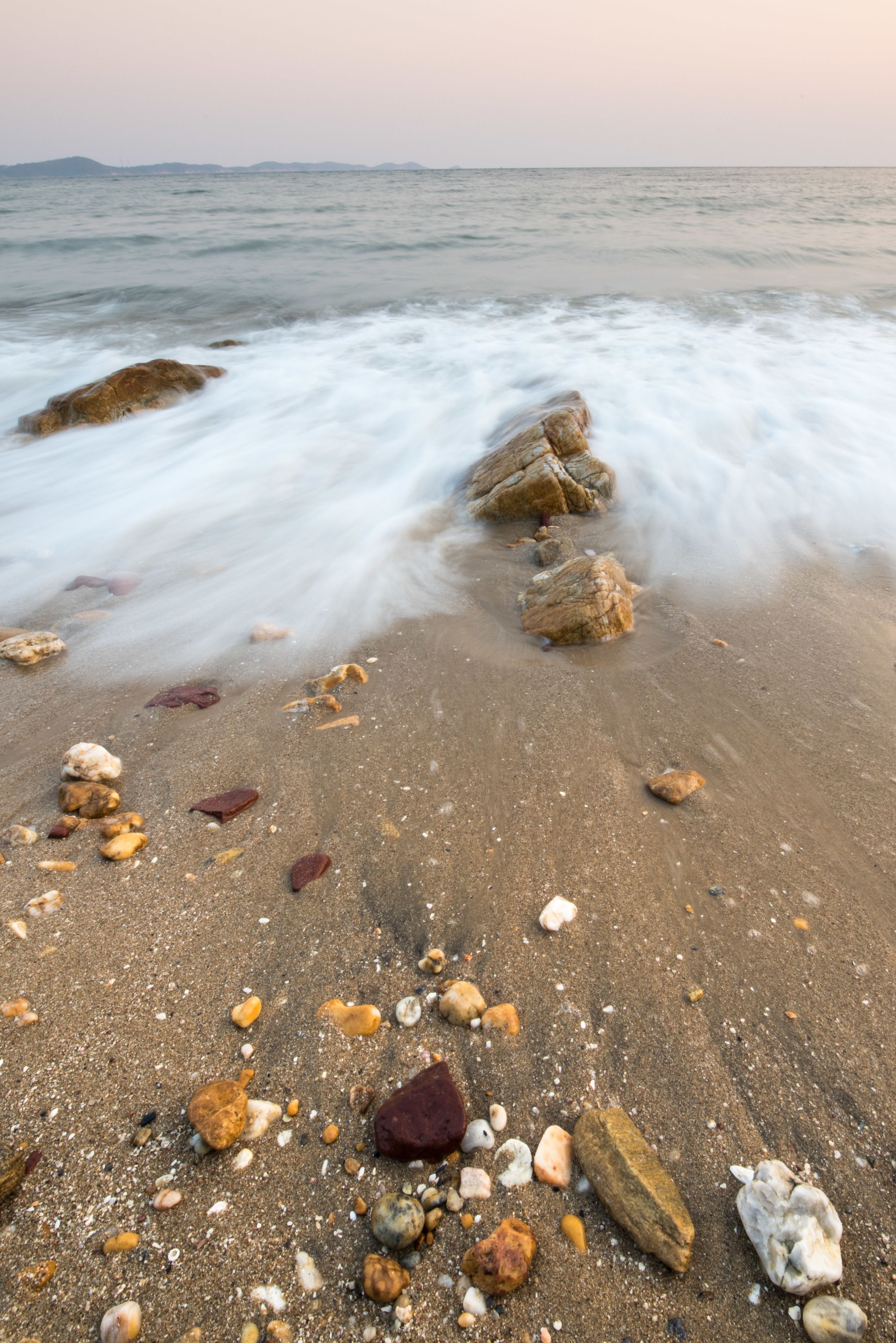 A beach with smooth, flowing water and scattered rocks.