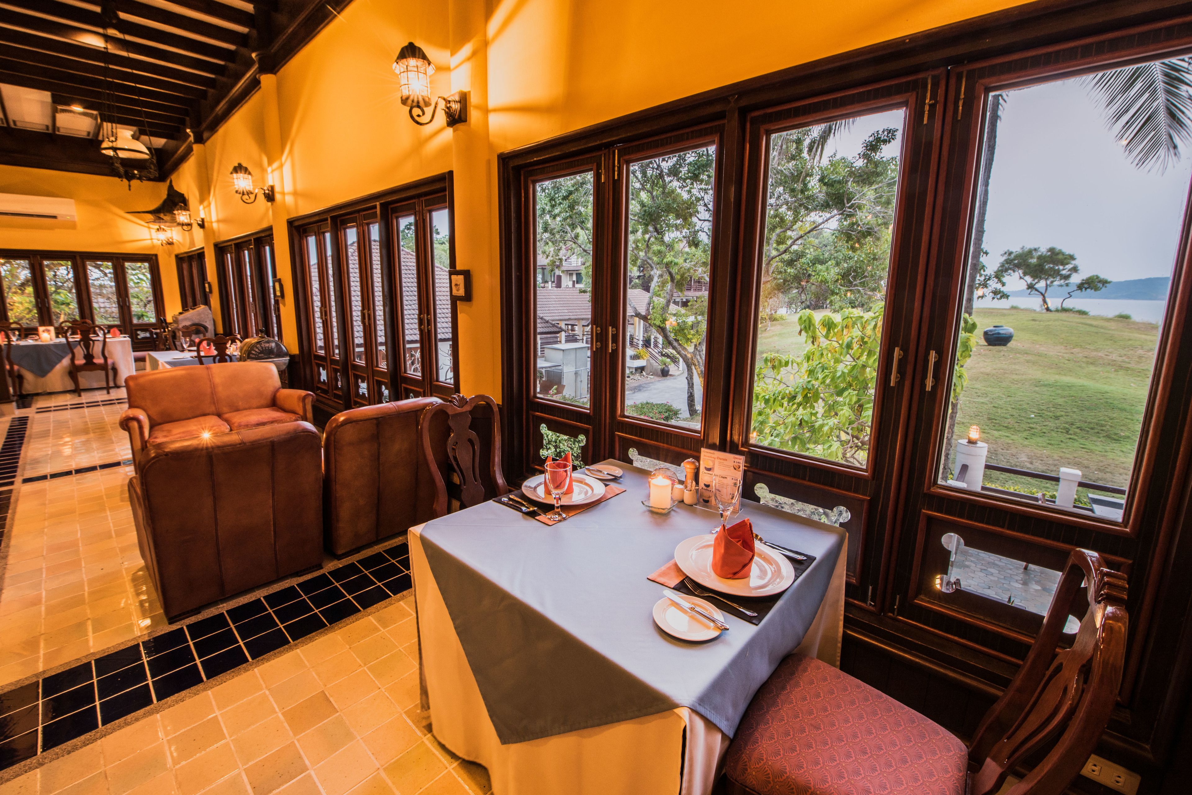 A restaurant with a table set for two, large windows with a view of the outdoors, and a tiled floor.