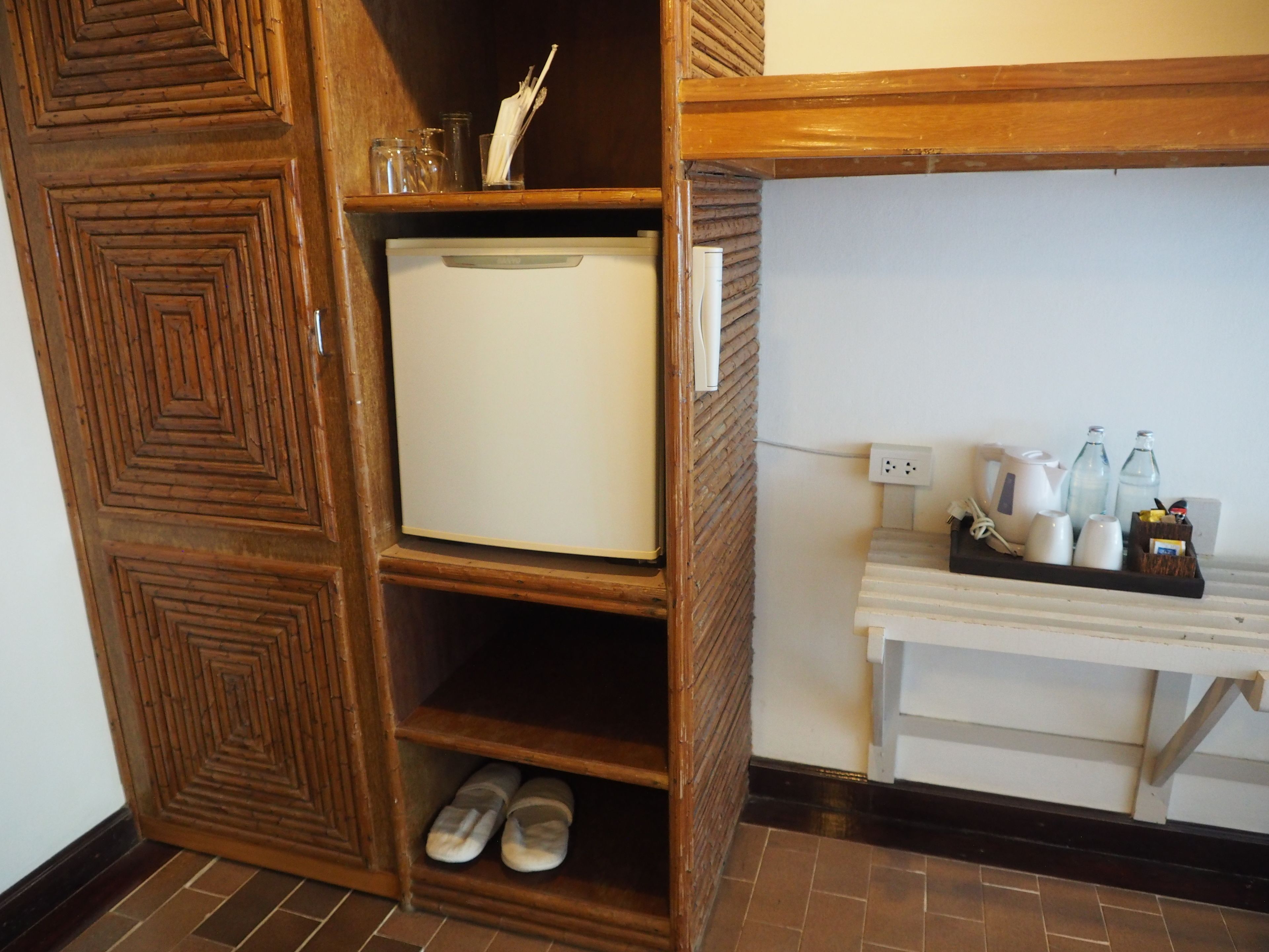 A compact kitchen with a built-in refrigerator, a small shelf with shoes, and a countertop with kitchenware.