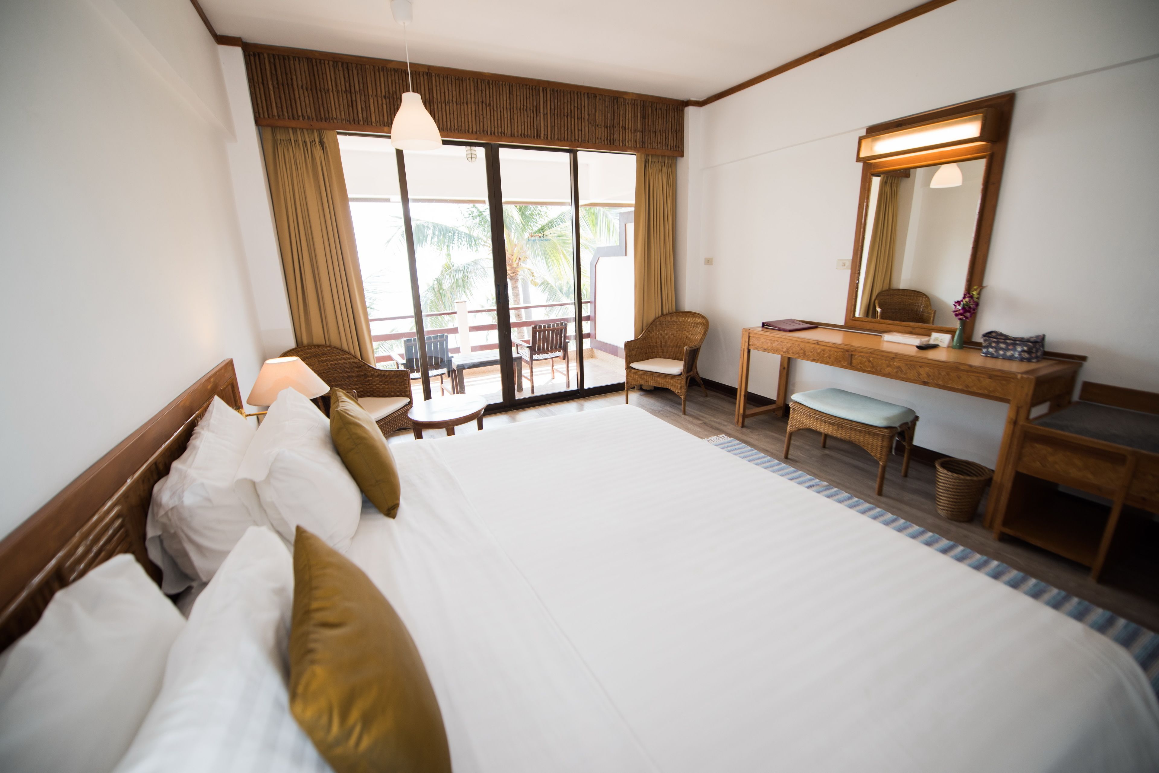 A hotel room with a large bed, a desk, a chair, a mirror, and a view of the outdoors.