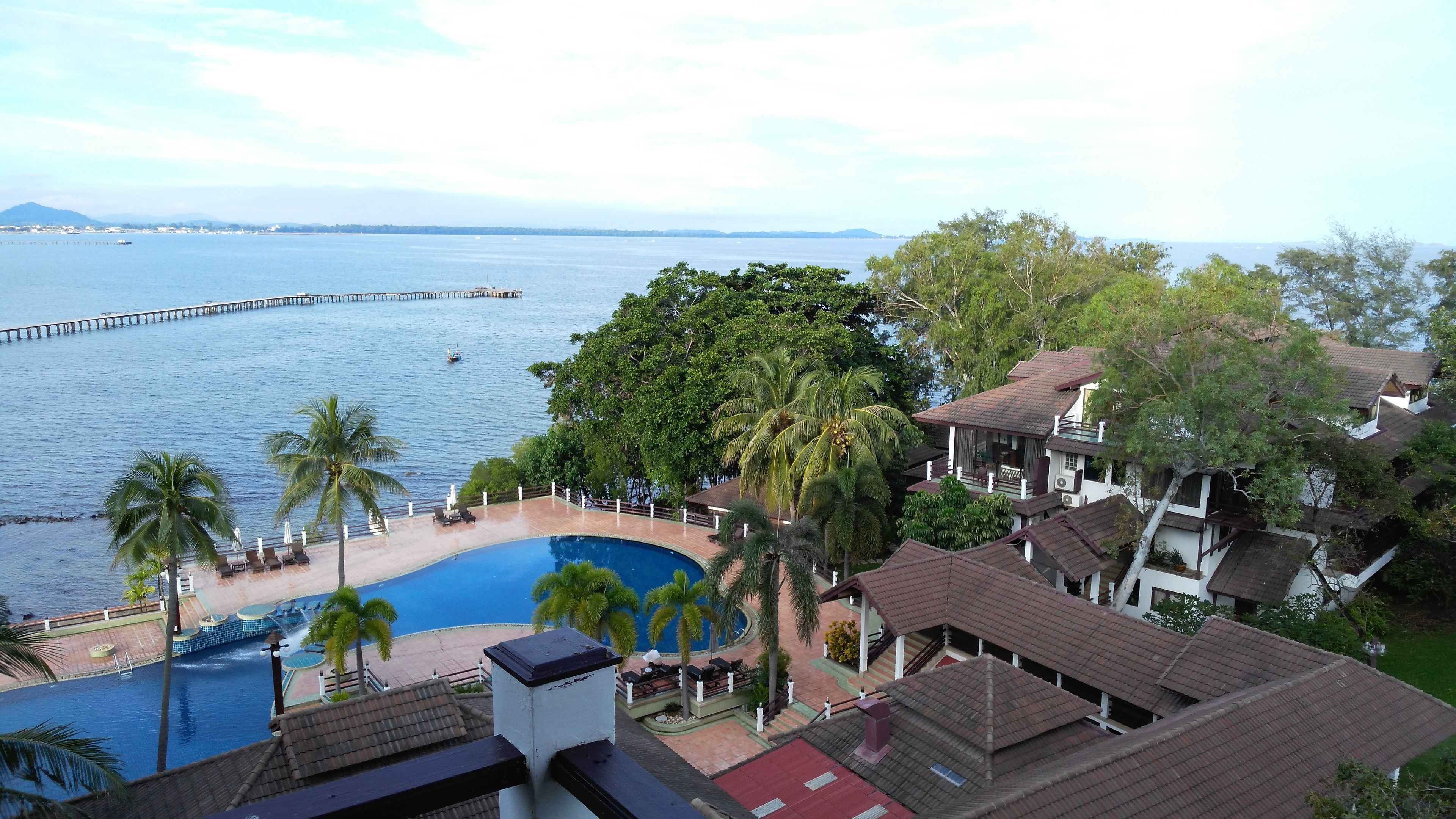 A resort with a swimming pool, palm trees, and a view of the sea.