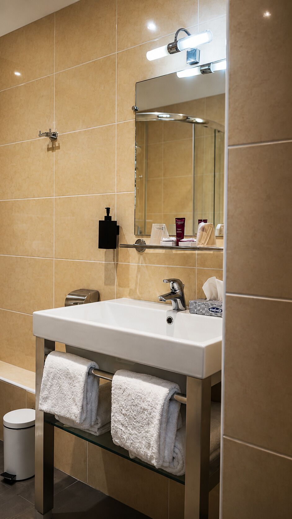 A bathroom with a white sink, a mirror, and two towels on a glass shelf.