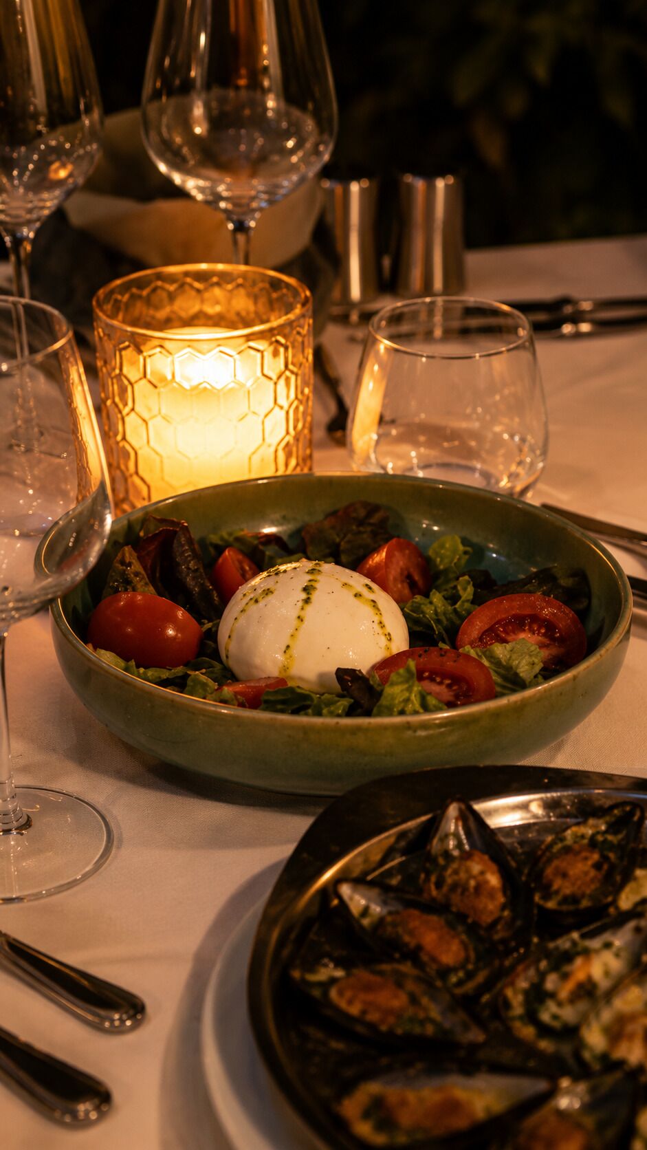 A dining table with a bowl of salad, a plate of mussels, and a lit candle.