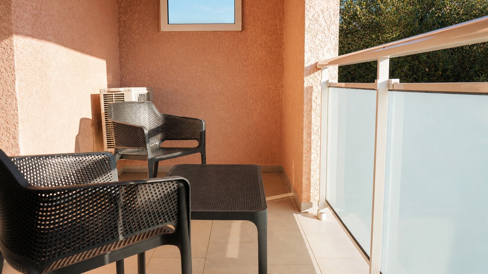 Een balkon met twee stoelen en een tafel, een lijst met een foto aan de muur, en een glazen balustrade.