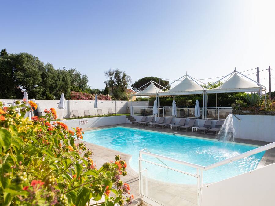 Una piscina con fuente, rodeada de sillones de descanso y sombrillas, bajo un cielo despejado.