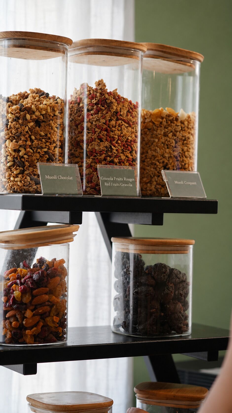 A shelf with multiple glass jars containing various granola and muesli mixes, each labeled with their respective names.