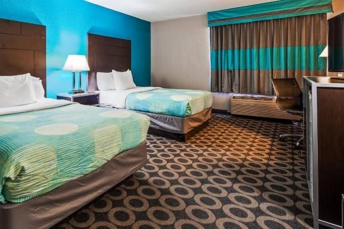 A hotel room with two beds, a desk, a chair, and a television.