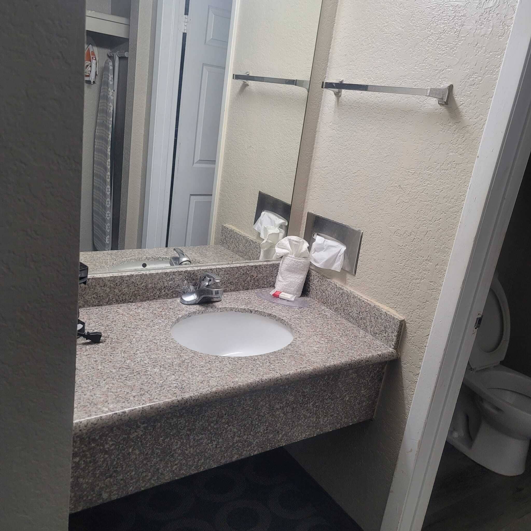 Un baño con lavamanos de encimera de granito, un espejo y dispensador de toallas.