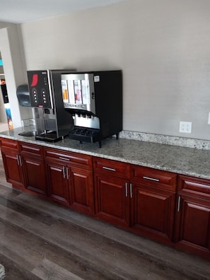 A kitchen with a built-in coffee machine, wooden cabinets, and a granite countertop. - Travelodge by Wyndham San Antonio Downtown Northeast (San Antonio)