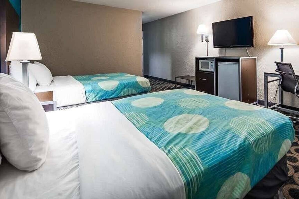 A hotel room with two beds, a desk, a television, and a chair.