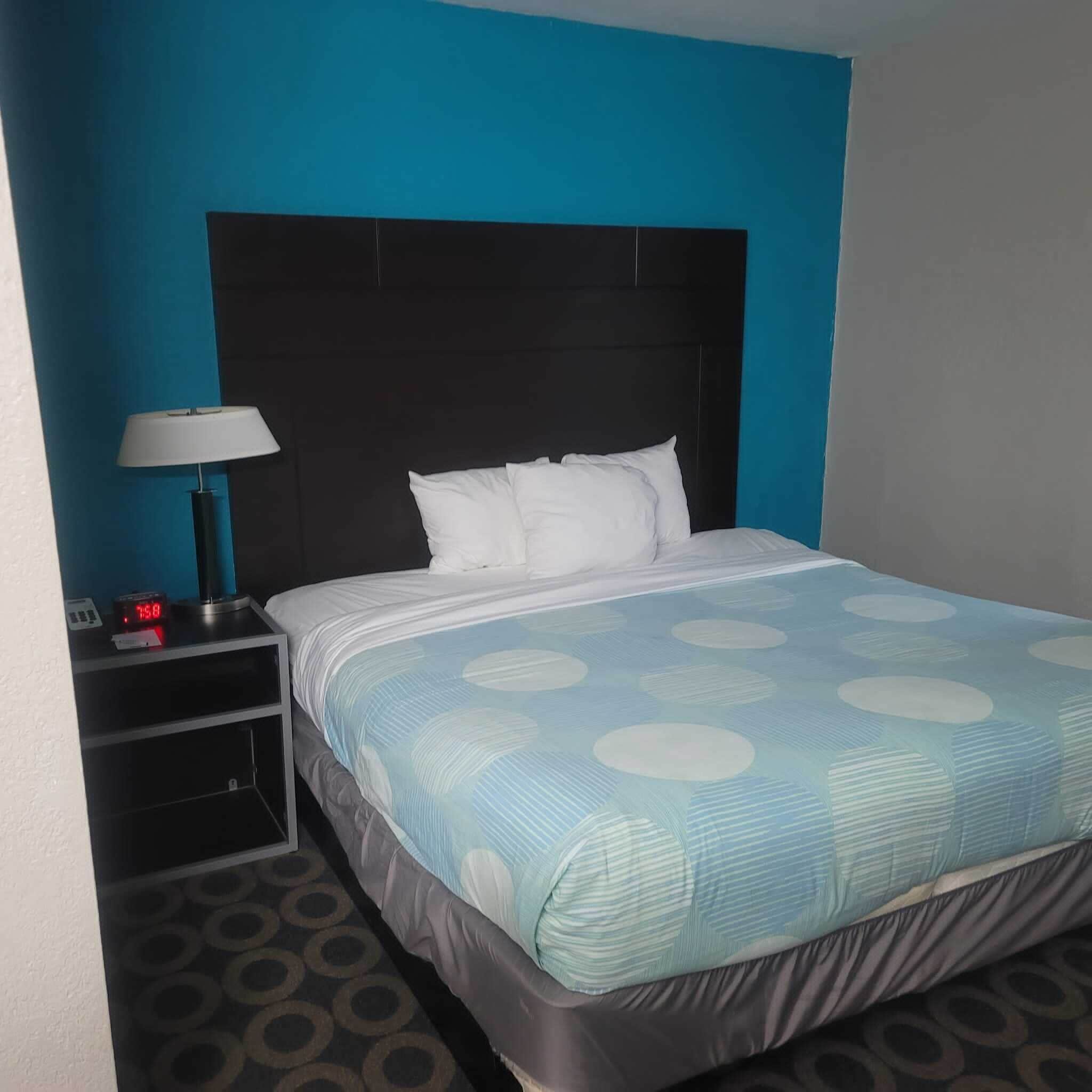 Ein Hotelzimmer mit einem Bett, einem Nachttisch mit Lampe und einer digitalen Uhr.