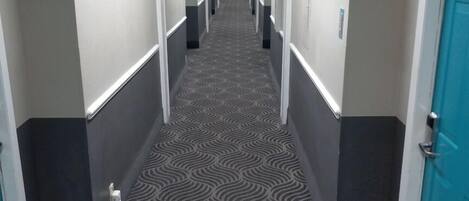Corredor de hotel com carpete estampado, paredes brancas e portas em ambos os lados.