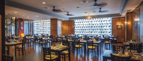 A spacious dining area with multiple tables and chairs, ceiling fans, and decorative wall panels.