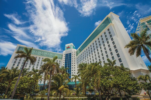 A multi-story hotel with a prominent 'R' logo on the top, surrounded by palm trees and a clear blue sky.
