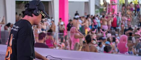 A DJ booth with a Pioneer DJ controller, a crowd in the background, and a pink column.
