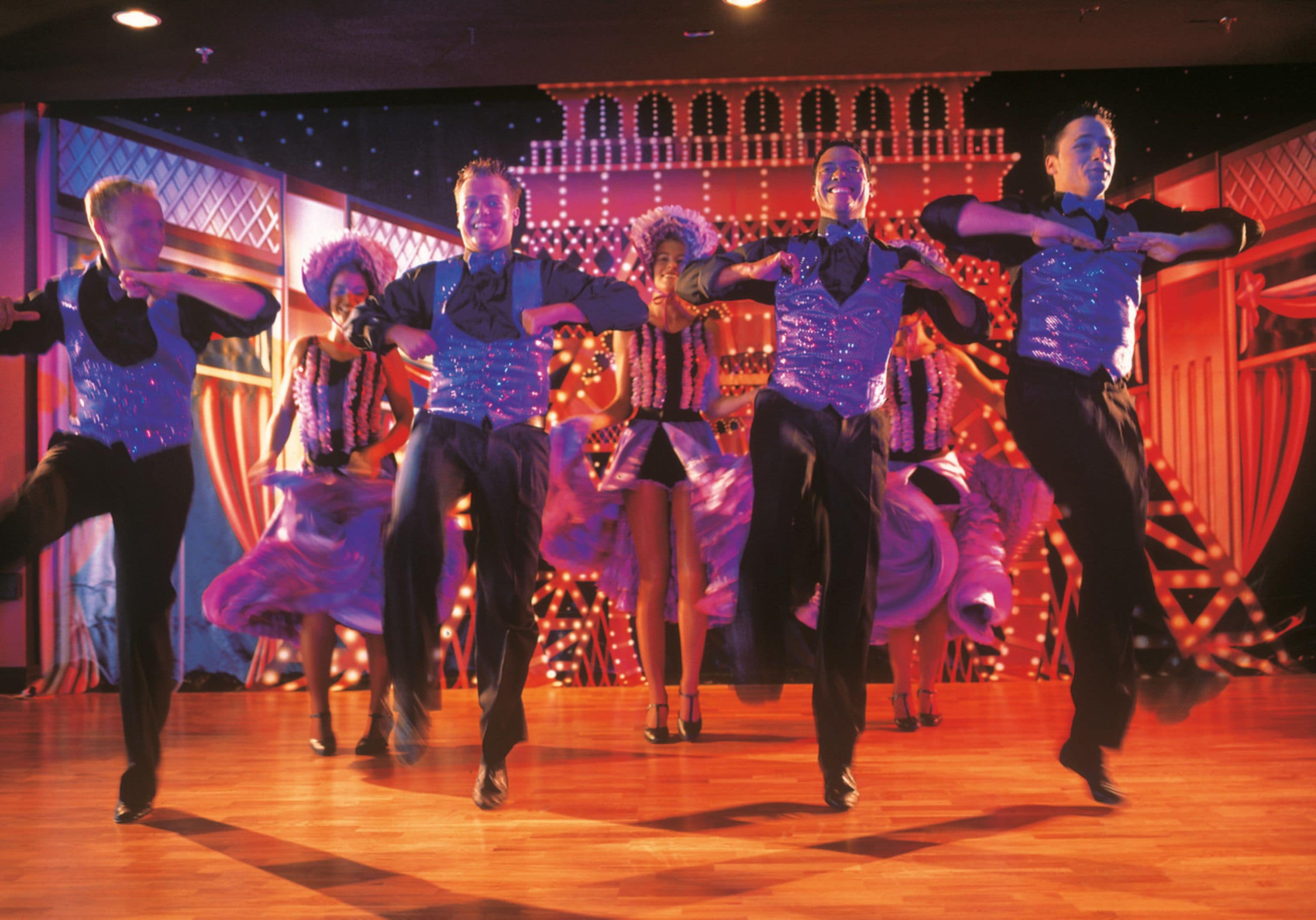 Un groupe de danseurs se produisant sur un plancher en bois, avec un décor en arrière-plan.