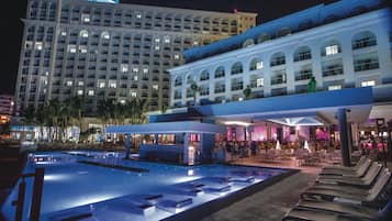 Un hotel con un amplio área de piscina, numerosas tumbonas y un bar.
