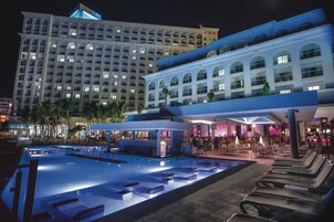 Un hotel con un amplio área de piscina, numerosas tumbonas y un bar.