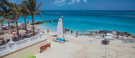 A beach with a white fence, palm trees, a sailboat, and a goalpost.