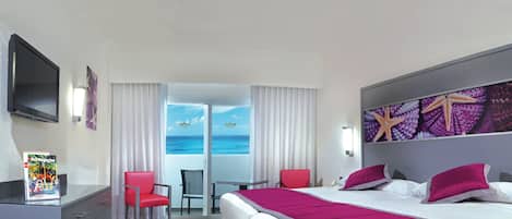 Habitación de hotel con cama, escritorio, silla, televisor y vista al océano.