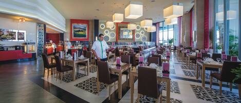 A spacious hotel lobby with multiple dining areas, a reception desk, and large windows offering views.
